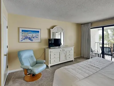 a bedroom with a bed and a chair and a television at Edgewater Villa 117 in Panama City Beach