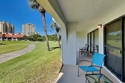 a porch with chairs and a lawn with palm trees at Edgewater Villa #602 in Panama City Beach