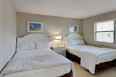 a bedroom with two beds and a lamp and a window at Edgewater Villa #604 in Panama City Beach