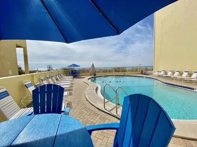 a pool with blue chairs and a table with an umbrella at Continental 503 in Panama City Beach