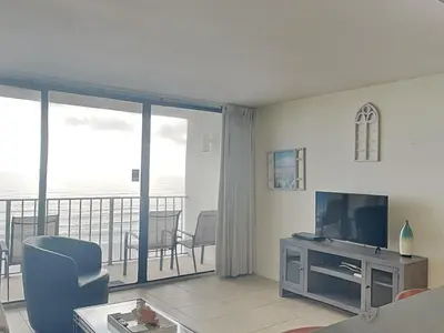 a living room with a couch and a television and a balcony at Edgewater Tower III #606 in Panama City Beach