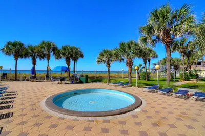 a pool with chairs and palm trees and the ocean at Summit Beach Resort #901 in Panama City Beach