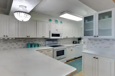 a white kitchen with white cabinets and a chandelier at Regency Towers 1202 in Panama City Beach