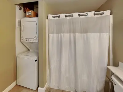a bathroom with a white shower curtain next to a washer at Shores of Panama #1111 in Panama City Beach