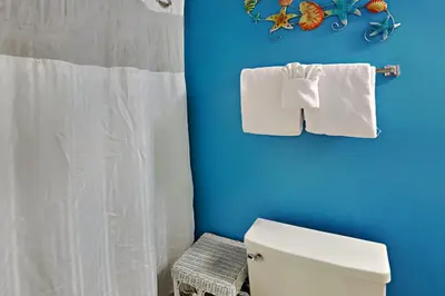 a bathroom with a blue wall and a toilet and towels at Edgewater Villa 1001 in Panama City Beach