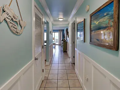 a hallway of a home with a tile floor and paintings on the walls at Edgewater Villa 1509 in Panama City Beach