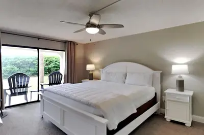 a bedroom with a white bed with two chairs and a window at Edgewater Villa #2301 in Panama City Beach