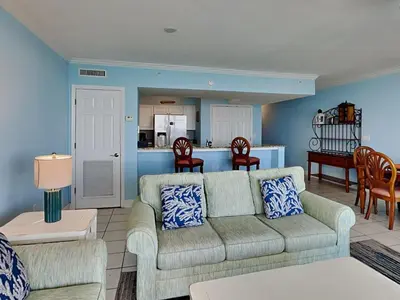 a living room with a couch and a kitchen at Emerald Beach #1127 in Panama City Beach