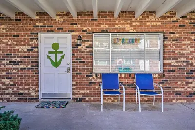 a brick building with two blue chairs and a door at Steps to Sand, Pool Access Cozy Panama City Condo in Panama City Beach