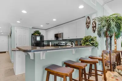 a kitchen with white cabinets and wooden bar stools at Majestic Beach Towers 2-1305 in Panama City Beach