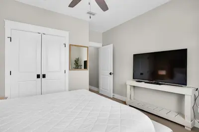a white bedroom with a large bed and a flat screen tv at Moonlight Cottage in Panama City Beach