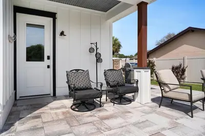 a porch with three chairs and a white door at Moonlight Cottage in Panama City Beach
