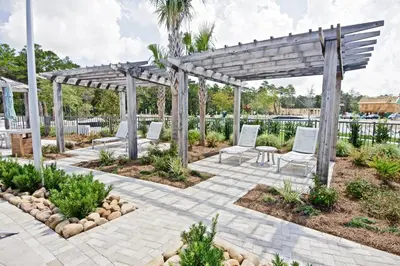a patio with white chairs under a wooden pergola at Beach Abode in Watersound Beach