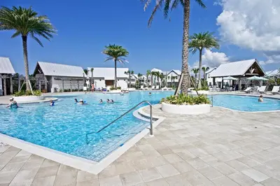 a large swimming pool with people in it with palm trees at Beach Abode in Watersound Beach