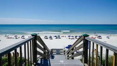 a wooden staircase leading to a beach with umbrellas at Villas At Sunset Beach A302 - Sunset Villa in Rosemary Beach