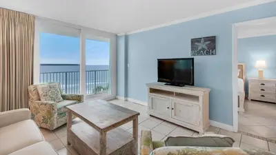 a living room with a television and a balcony with the ocean at Beachcrest 406 in Santa Rosa Beach