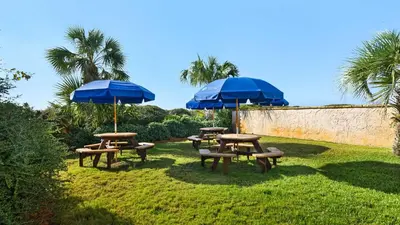 three picnic tables with blue umbrellas on the grass at Beachcrest 406 in Santa Rosa Beach