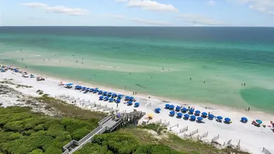 a beach with blue and white umbrellas and the ocean at Beachcrest 1005 in Santa Rosa Beach