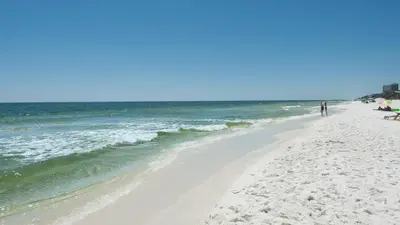 a beach with a person walking on the sand and the ocean at Moon Glow in Santa Rosa Beach