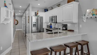 a kitchen with white cabinets and a counter with stools at Monterey Condos A302 in Panama City Beach