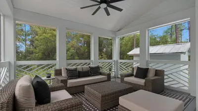 a screened in porch with furniture and windows at Resting Beach Face in Rosemary Beach