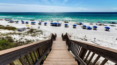 a wooden boardwalk leading to a beach with umbrellas and chairs at Palms A3 in Santa Rosa Beach