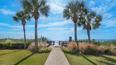 a pathway with palm trees and a bench and the ocean at Palms C5 in Santa Rosa Beach