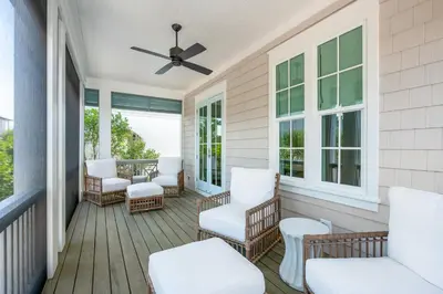 a screened porch with white chairs and a ceiling fan at Maison de Joie in Inlet Beach