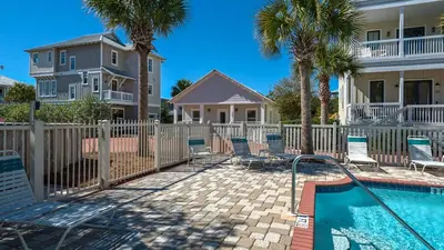 a pool with chairs and a fence with palm trees at Quietude in Santa Rosa Beach
