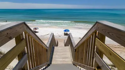 a wooden stairway leading to a beach with umbrellas at Sago Sands 402 in Santa Rosa Beach