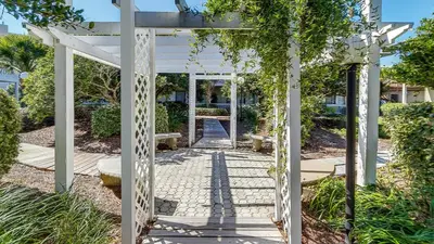 a white pergola in a garden with a walkway at Beachwood Villas 3A in Santa Rosa Beach