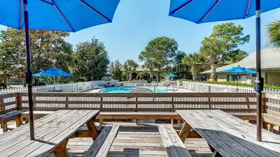 two picnic tables with umbrellas in front of a pool at Beachwood Villas 4C in Santa Rosa Beach