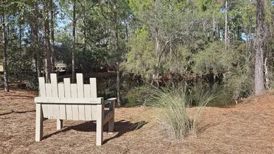 a white bench sitting in front of a forest at Crow's Nest in Santa Rosa Beach
