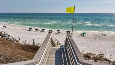 a staircase leading to a beach with a yellow flag at Float Away in Panama City Beach