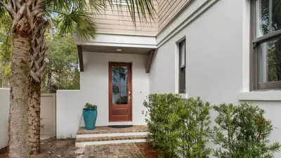 a white house with a red door and a palm tree at Ocean Park in Santa Rosa Beach