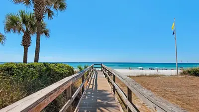 a wooden boardwalk leading to the beach with palm trees at Seabreeze in Panama City Beach