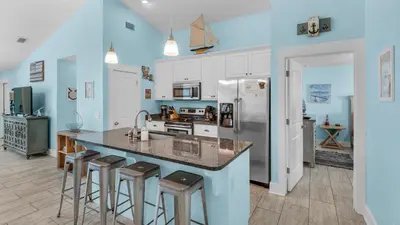 a kitchen with a counter with stools and a refrigerator at Sandy Teauxs in Panama City Beach