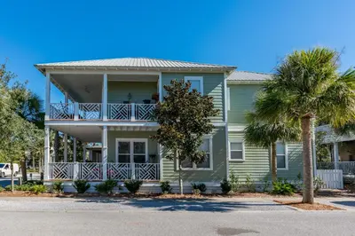 a green house with a balcony and palm trees at Shore Thing in Rosemary Beach