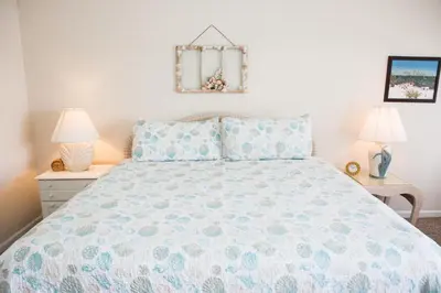 a bedroom with a bed with a blue comforter and two lamps at All's Well in Santa Rosa Beach