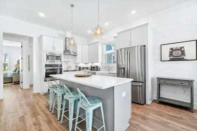 a kitchen with white cabinets and a kitchen island with stools at 30A Beach House - Mira Bella in Rosemary Beach