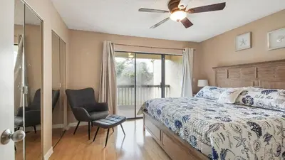a bedroom with a bed and a chair and a window at Beach Walk 10C by Sand Seeker Vacations in Panama City Beach