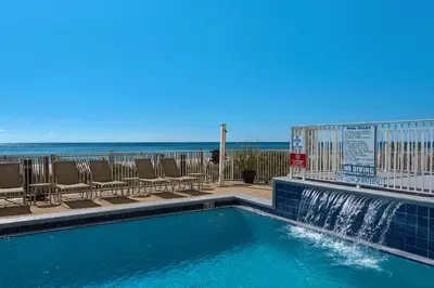a swimming pool with a waterfall and chairs and the beach at Emerald Isle 1201 in Panama City Beach