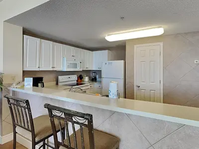 a kitchen with white cabinets and a counter with two chairs at Majestic Beach Towers I #913 in Panama City Beach