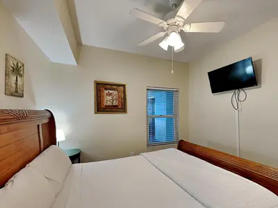 a bedroom with a bed with a ceiling fan and a flat screen tv at Majestic Beach Towers II #1006 in Panama City Beach