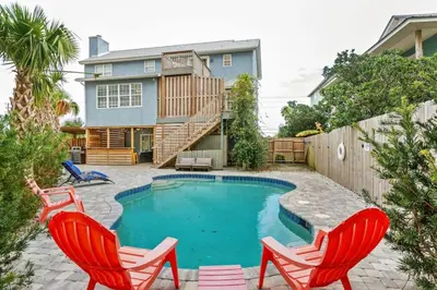 a swimming pool with two red chairs and a house at Sand Castle-Pool, Game Rooms, covered outdoor space with tiki bar, 1min walk to beach in Panama City Beach