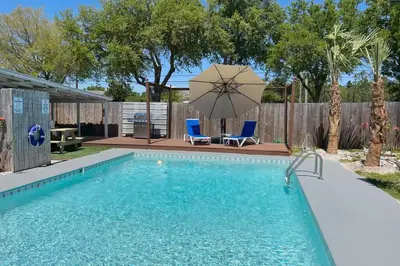 a swimming pool with a umbrella and two chairs and a table at Flirty Flamingo with Private Heated Pool, Game Room, and AMAZING Covered Outdoor Living in Panama City Beach