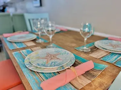 a wooden table with plates and wine glasses on it at Beach Haven - Seasonal Hot Tub, Fire Pit, BBQ, 700 Feet to Beach, Central PCB, FREE Daily Activities, & More! in Panama City Beach