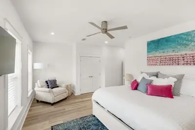 a white bedroom with a large bed and a chair at The Eagles Nest in Rosemary Beach