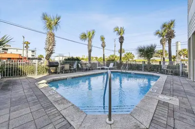 a swimming pool with palm trees and a fence at Second Wind by Book That Condo in Panama City Beach