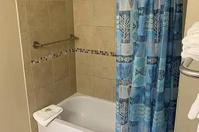 a bathroom with a tub and a blue shower curtain at Origin at Seahaven in Panama City Beach